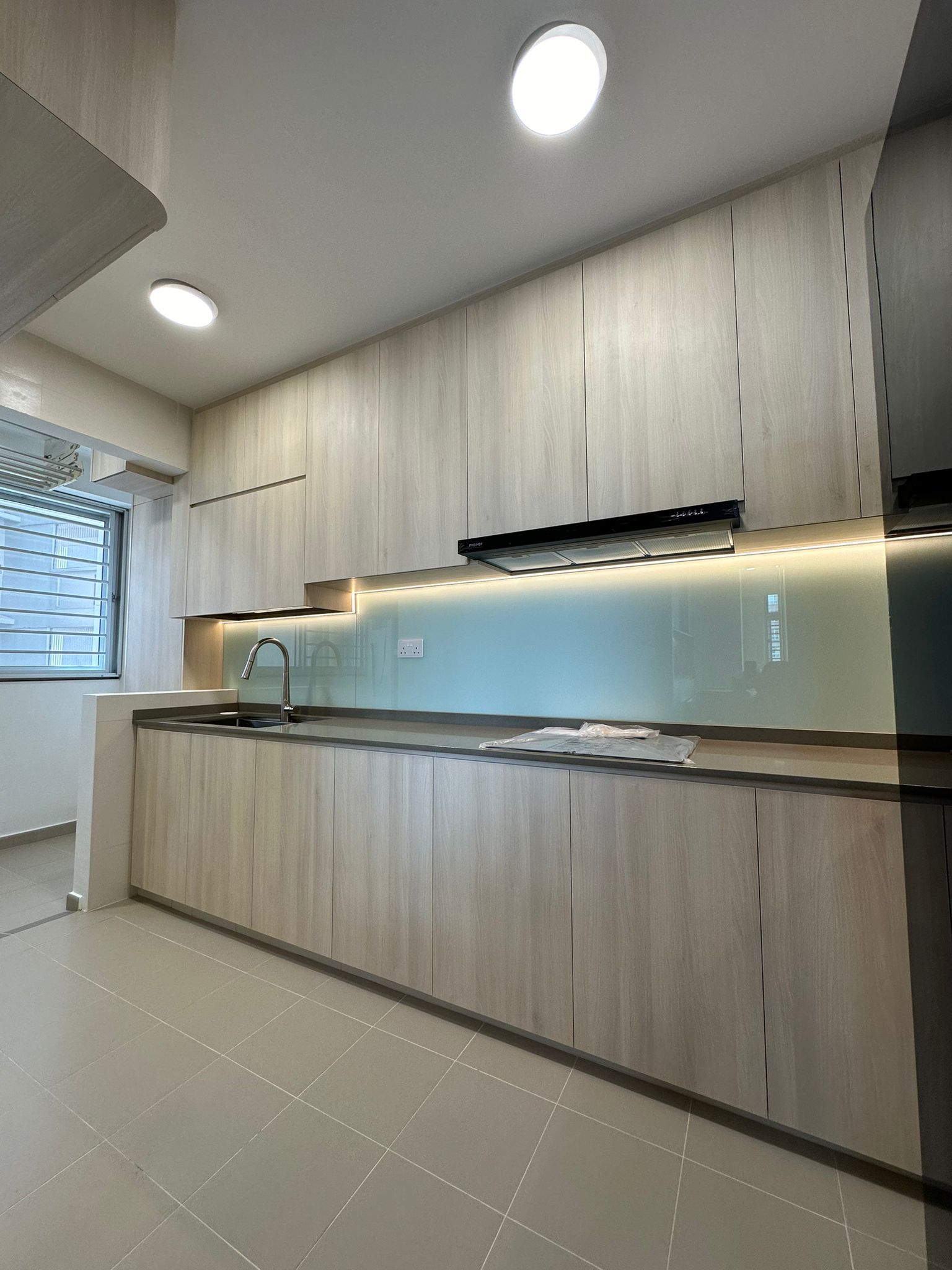 Blk292B Bukit Batok East Ave 6 Kitchen Interior Design 1 The kitchen design is both functional and visually appealing, featuring a custom-made L-shaped, full-width, full-height cabinet that maximizes storage and efficiency. The light wood color tiles not only complement the overall design but also enhance hygiene, making cleaning effortless. Bright LED downlights on the ceiling ensure the space is well-lit, creating a vibrant and welcoming environment that's perfect for cooking and gathering.